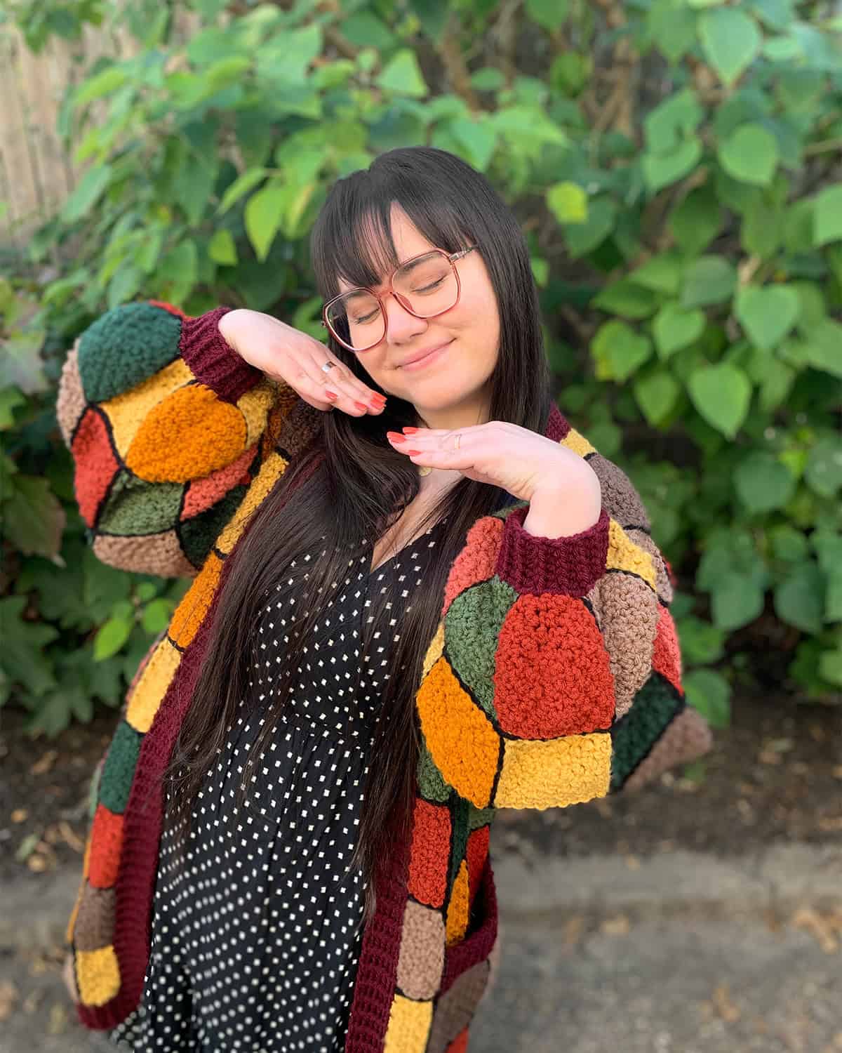 Joey Diehl, the designer of Virkadia crochet patterns, posing outside wearing a crochet patchwork cardigan